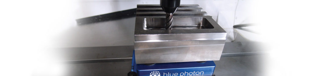 Photo of a drill press drilling a hole into a metal part, held in place by Blue Photon light-activated adhesive